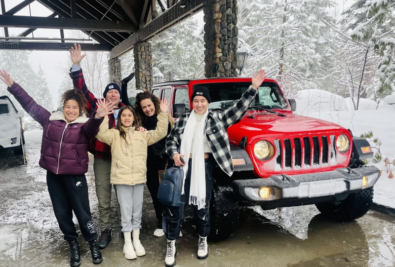 A family with a red Jeep on a snowy mountain road.